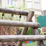 Wooden playground climbing frame with red rope nets in a residential park area.