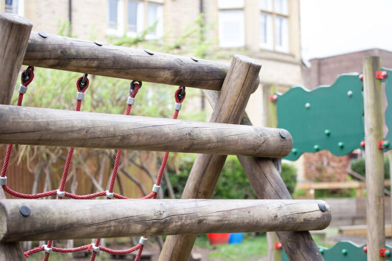 Wooden playground climbing frame with red rope nets in a residential park area.