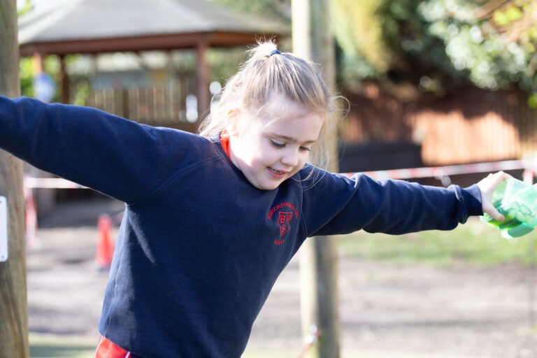 Young girl in a navy hoodie with arms outstretched at a playground, smiling.