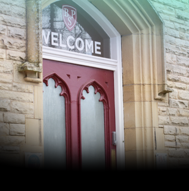 Stone entryway with red arched double doors and a 'WELCOME' sign above; a crest with the letters BPS appears in the upper window.