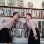 2 girls reciting a poem behind a wall of books